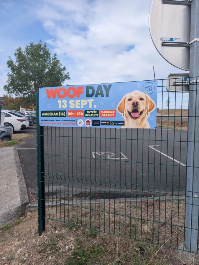 Banderole Woof Day avec logos sponsors, sur un grillage près d'un parking